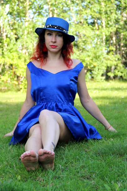 一个红头发的女人，戴着一顶蓝色的帽子，穿着一件蓝色的短裙，赤着脚坐在草坪上图片下载