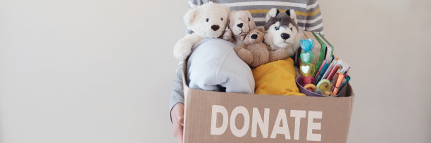 一个十几岁的小男孩拿着一个箱子，里面装满了用来捐赠的玩具、衣服、书籍和文具图片下载