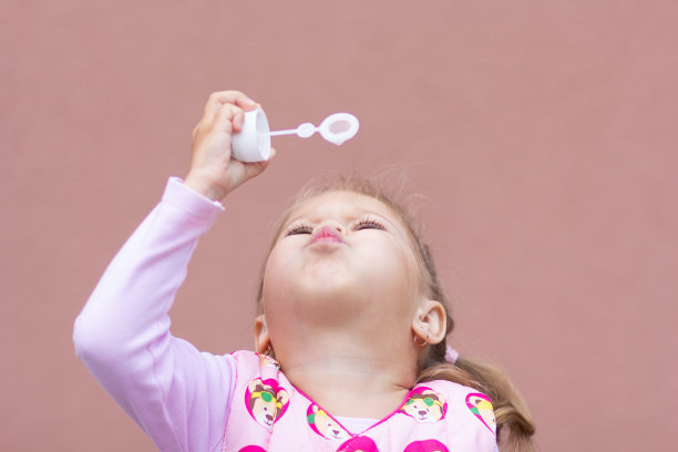 肖像的小女孩吹肥皂泡在粉红色的背景图片下载