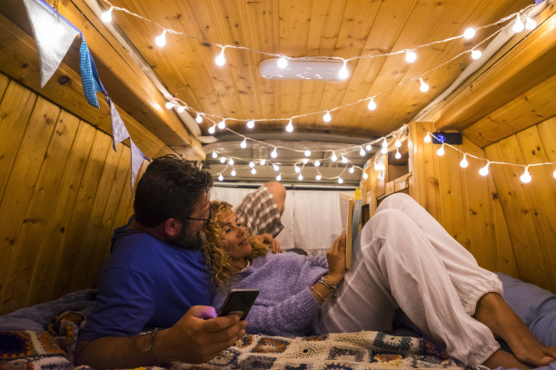 旅行和浪漫的夜晚在一个木制的修复美丽的货车在爱的幸福的成年高加索夫妇放松与电话和纸质书-旅游和旅行者在一起的人图片下载