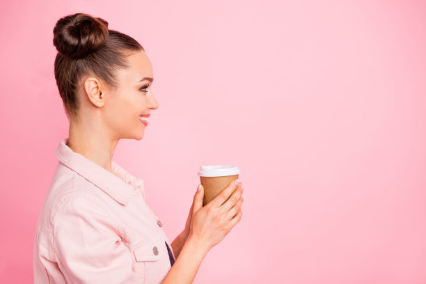简介侧面照片，快乐的千禧拿着杯与卡布奇诺微笑穿着夹克孤立在粉红色的背景图片下载