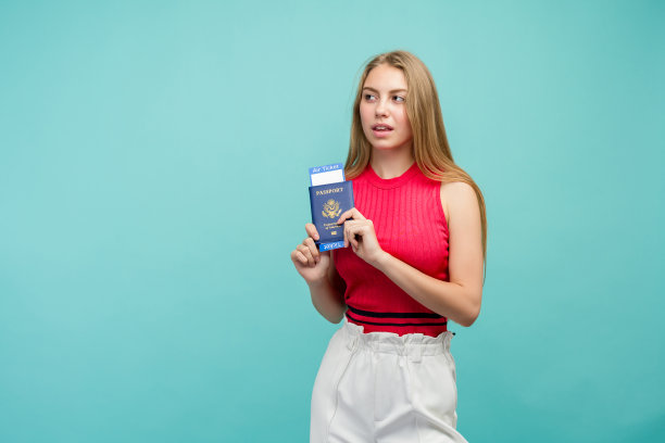 一名年轻漂亮的女学生拿着护照和门票的照片。孤立在明亮的蓝色背景。图片下载