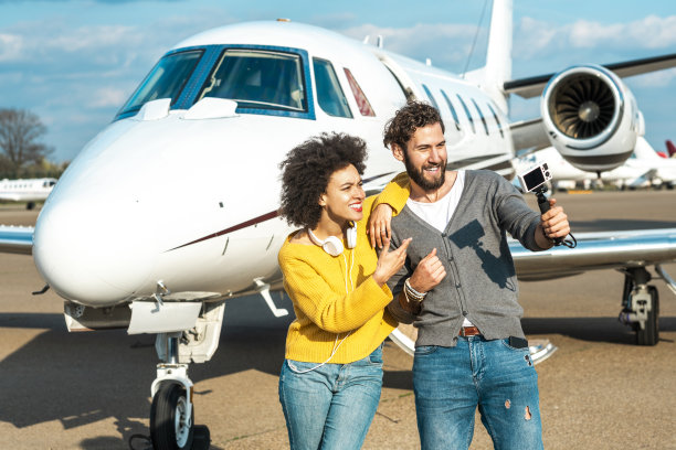 一对Vlogger夫妇在一架停在机场跑道上的私人飞机的头锥旁一起创作内容图片下载