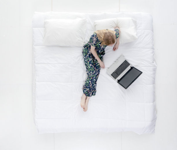 正上方的视图/完整的长度/一个20-29岁的成年美丽的白人女性/年轻女性坐在卧室的白色背景穿着睡衣谁是工作到很晚谁是工作和使用笔记本电脑/电脑图片下载