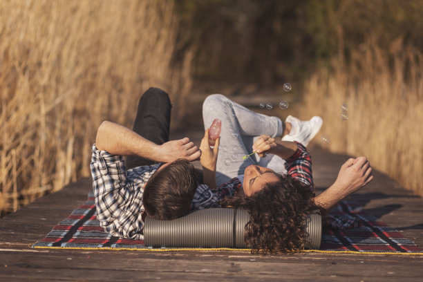 一对夫妇在湖边码头上吹肥皂泡野餐图片下载