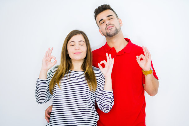 年轻美丽的夫妇一起在白色孤立的背景放松和微笑，闭上眼睛做冥想手势与手指。瑜伽的概念。图片下载