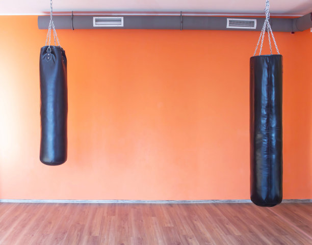 体育和武术的沙袋挂在体育馆的橙色墙的背景下，复制空间图片下载