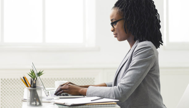 坐在办公室里用笔记本电脑打字的黑色办公室女孩图片下载