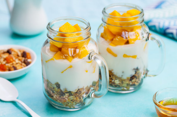 新鲜的芒果，酸奶和格兰诺拉麦片装在罐子里。蓝石头背景。关闭了。图片下载