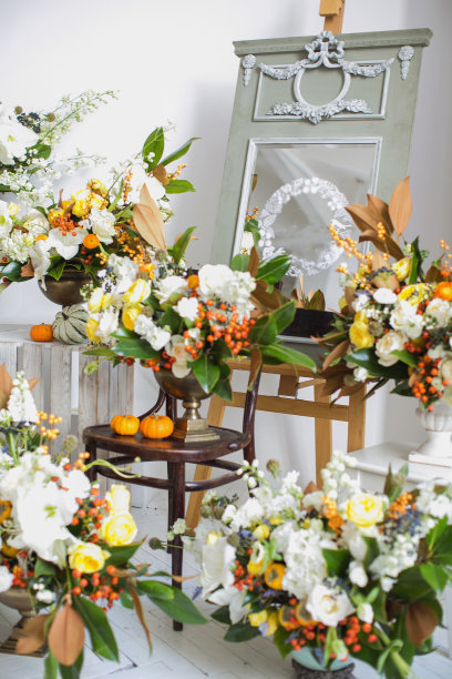 许多青铜花瓶，里面有一束百合、牡丹、玫瑰、口水珠和绿叶，还有柿子和红浆果。秋天心情，橙色南瓜。装饰婚礼或花店。图片下载