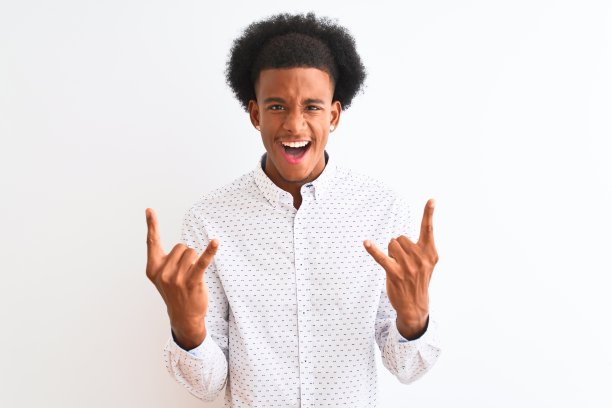 年轻的非洲裔美国人穿着优雅的衬衫站在孤立的白色背景大喊与疯狂的表情做摇滚符号与手举起。音乐明星。沉重的概念。图片下载