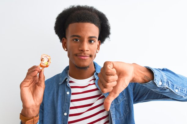 年轻的非洲裔美国人在孤立的白人背景下用筷子吃寿司，愤怒的脸，消极的标志表示不喜欢，拇指朝下，拒绝的概念图片下载