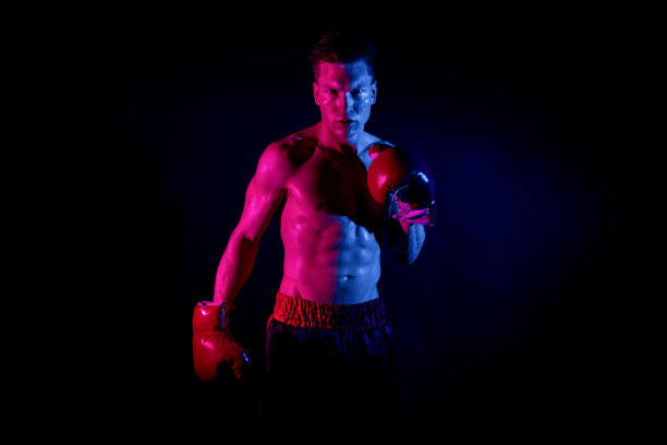 上腰/一人/正面观看20-29岁英俊的白人男性/年轻男子前面的黑色背景，戴着拳击手套，肌肉发达/性别象征/赤裸上身/严肃/自信/专注和拳击图片下载