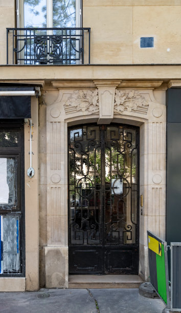 欧洲城市街道上的古董门，带有镜面玻璃窗。黑色的门与华丽的金属格子和模糊的反射。建筑外部有老式格栅阳台，靠近石屋窗户图片下载