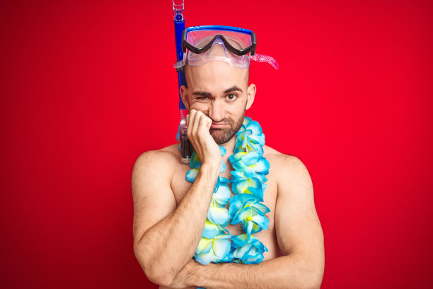 年轻男子戴着潜水镜和夏威夷花环在孤立的红色背景下思考看起来疲倦和厌倦的抑郁问题交叉双臂。图片下载
