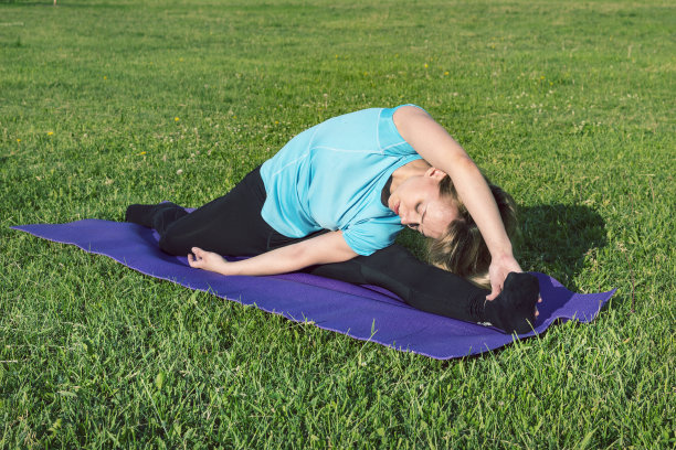 关于一个年轻女子做瑜伽运动做鬼脸的有趣照片。以自然为背景的智能手机健身女孩，喜欢运动训练，在瑜伽垫上和绿色草地上锻炼图片下载