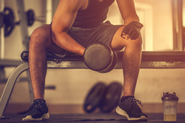 健美运动员在健身房用哑铃锻炼。健美运动员用哑铃锻炼。健身肌肉的身体图片下载