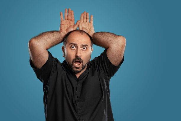 近距离的肖像一个黑发的中年男子的胡子，穿着黑色t恤和摆姿势的蓝色背景图片下载