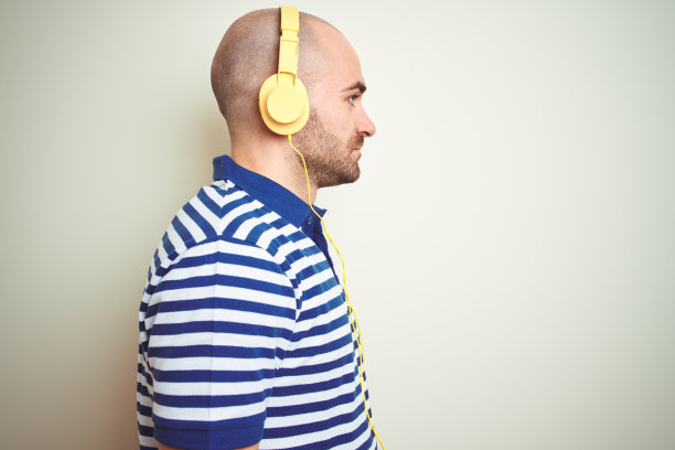 年轻人听着音乐戴着黄色耳机孤立的背景看向一边，放松的侧面姿势，自然的脸上带着自信的微笑。图片下载