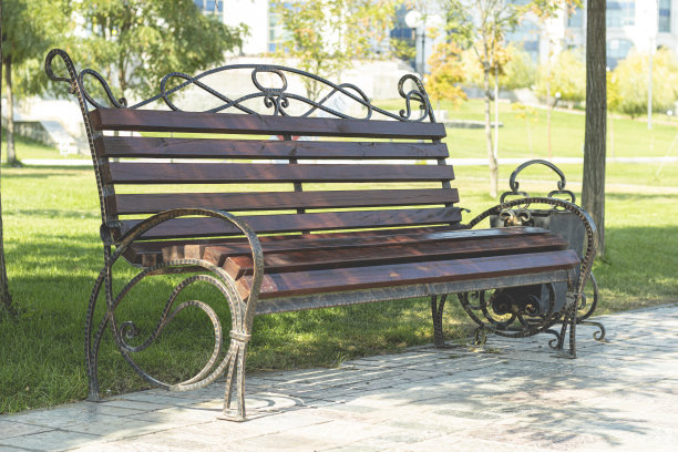 游乐园的木制长凳和金属艺术锻造。绿色的大自然背景上的棕色长凳。图片下载