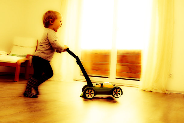 2岁的小男孩一边玩着他的玩具割草机一边在房间里尖叫和奔跑图片下载