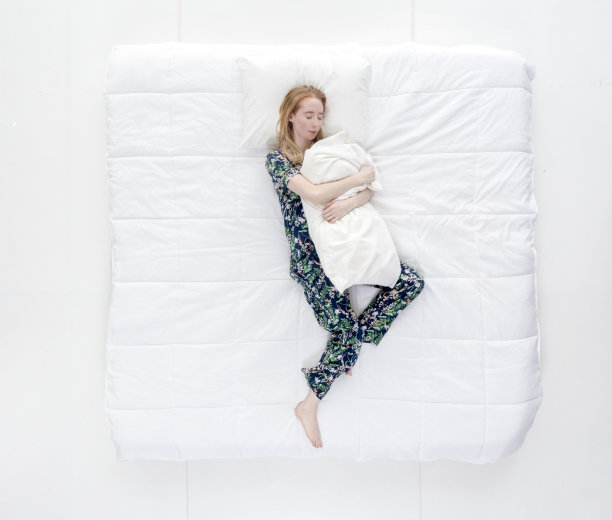 上图/全身/一个20-29岁的成年美丽的白人女性/年轻女性躺下/打盹/睡觉/放松/休息在卧室的白色背景下穿着睡衣拥抱图片下载