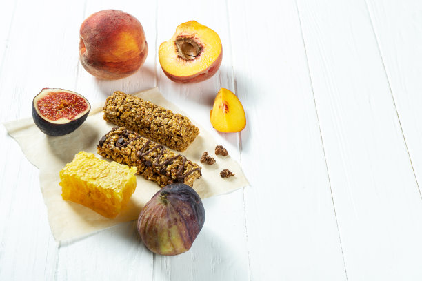 近距离格兰诺拉麦片酒吧与蜂蜜和无花果，桃在牛皮纸上的白色木制背景。健康的甜食点心。什锦麦片能量棒。格兰诺拉麦片当早餐。本空间图片下载