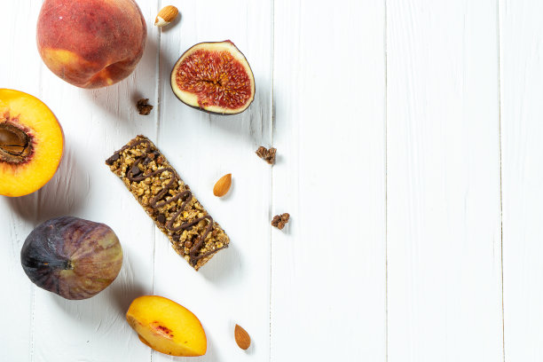 近距离格兰诺拉麦片酒吧与蜂蜜和无花果，桃在牛皮纸上的白色木制背景。健康的甜食点心。什锦麦片能量棒。格兰诺拉麦片当早餐。本空间图片下载