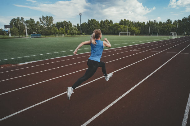 年轻的健身女运动员在跑道上跑步。田径场上的运动员。图片下载