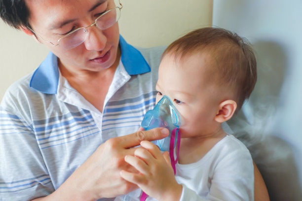 一位亚洲父亲用吸入器面罩帮助蹒跚学步的儿子进行吸入疗法图片下载