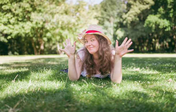 美丽的，微笑的女人躺在草地上，在绿色的公园。图片下载