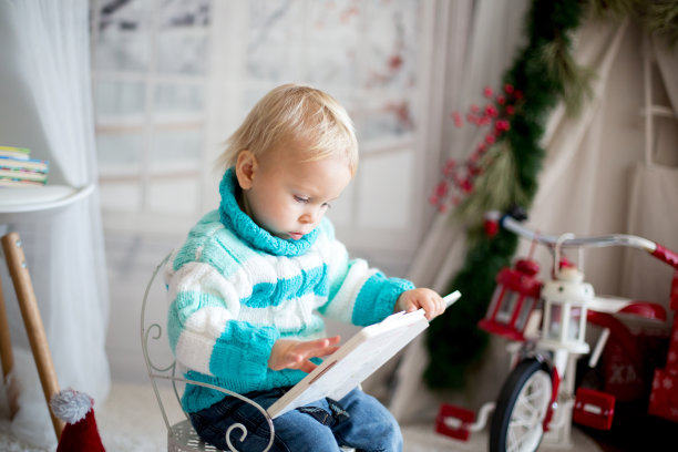 一个可爱的蹒跚学步的孩子在一个下雪的冬天在家里拿着彩色的书图片下载