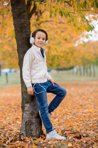 一个学龄前的孩子在秋天的公园里用耳机和手机听音乐的甜蜜肖像图片下载