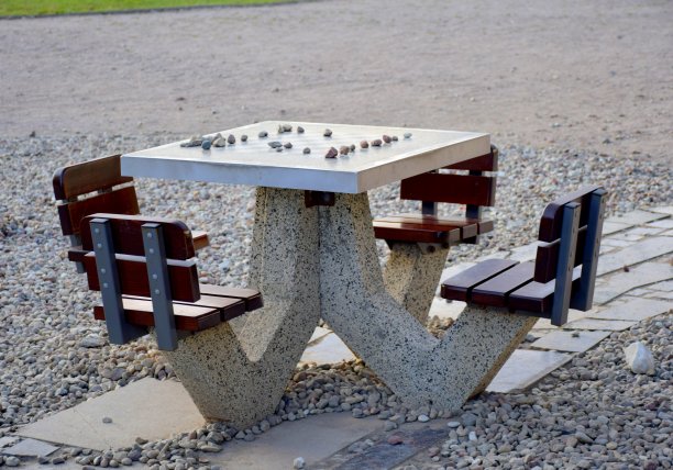 在公园中央的一条小路旁，有一张石桌，周围有四张木凳，桌面上刻着一个棋盘，还有许多用作棋子的小石头图片下载