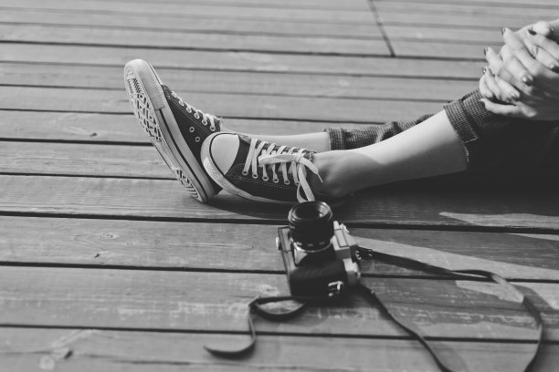 女性的腿在时髦的运动鞋和复古相机在户外木制表面，作物照片。黑白照片图片下载