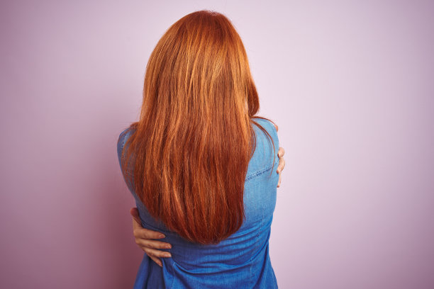 美丽的红发女人穿着牛仔衬衫和条纹t恤，孤立的粉红色背景拥抱自己快乐和积极的向后。爱自己，关心自己图片下载