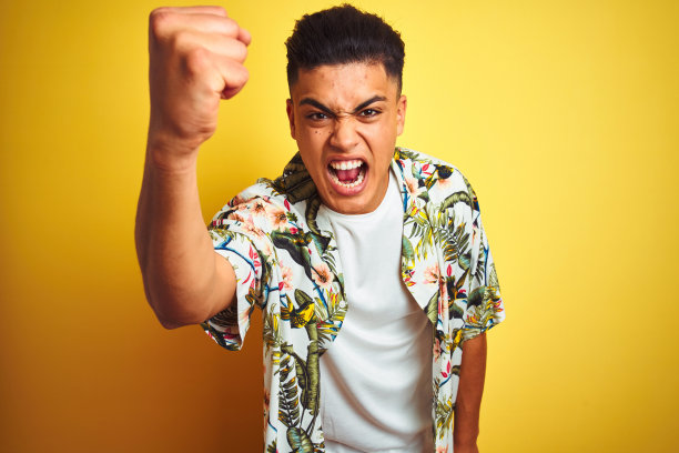 年轻的巴西人度假穿着夏天的花衬衫在孤立的黄色背景愤怒和疯狂举起拳头沮丧和愤怒，而大喊与愤怒。愤怒和侵略性的概念。图片下载