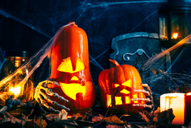 万圣节的装饰，杰克的灯笼带发光的眼睛，神秘的光芒，蜘蛛网，干燥的树叶，黑暗的背景，燃烧的蜡烛，骨骼图片下载