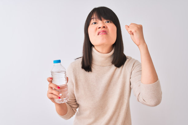 年轻美丽的中国女人拿着一瓶水，在孤立的白色背景下愤怒和沮丧的大喊大叫，疯狂地举起手，愤怒的概念图片下载