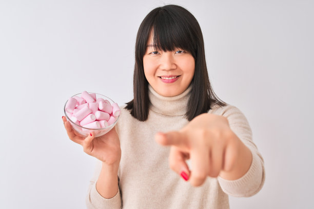 美丽的中国女人拿着碗和棉花糖在孤立的白色背景指向相机和你，手势，积极和自信的手势从前面图片下载