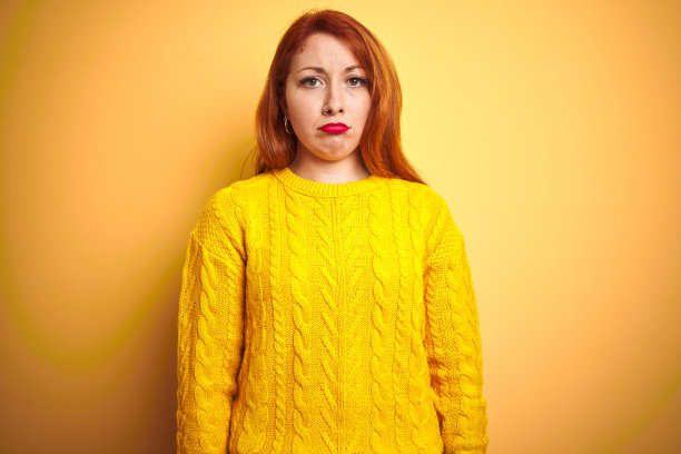 美丽的红发女人穿着冬季毛衣站在孤立的黄色背景沮丧和担心的痛苦，哭泣愤怒和害怕。悲伤的表情。图片下载