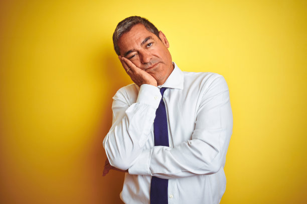 英俊的中年商人站在孤立的黄色背景思考看起来疲倦和厌倦的抑郁问题交叉双臂。图片下载