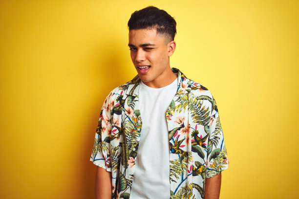 年轻的巴西男子度假穿着夏天花衬衫孤立的黄色背景眨着眼睛看着相机与性感的表情，愉快和快乐的脸。图片下载