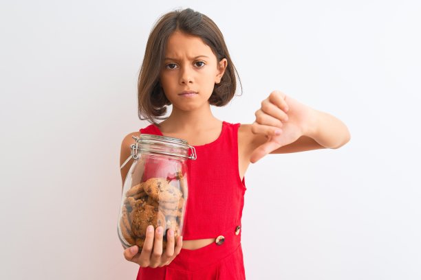 美丽的小女孩拿着一罐饼干站在孤立的白色背景下，愤怒的脸，消极的标志表示不喜欢，拇指朝下，拒绝的概念图片下载