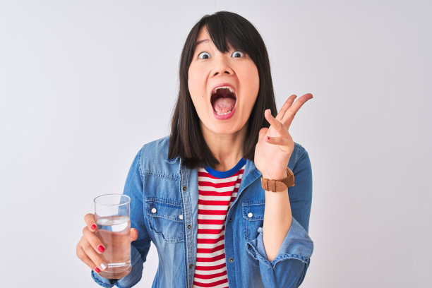 年轻美丽的中国女人拿着一杯水在孤立的白色背景非常高兴和兴奋，胜利者的表情庆祝胜利尖叫着大大的微笑和举起手图片下载