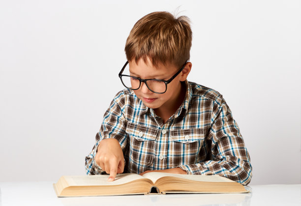 可爱的小男孩拿着书坐在书桌前。七岁的孩子图片下载