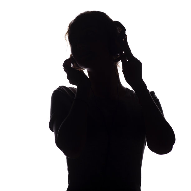 一个快乐女孩的剪影听着歌曲和放松在耳机里，十几岁的身影移动到一个白色的孤立的背景音乐，青年的生活方式的概念图片下载