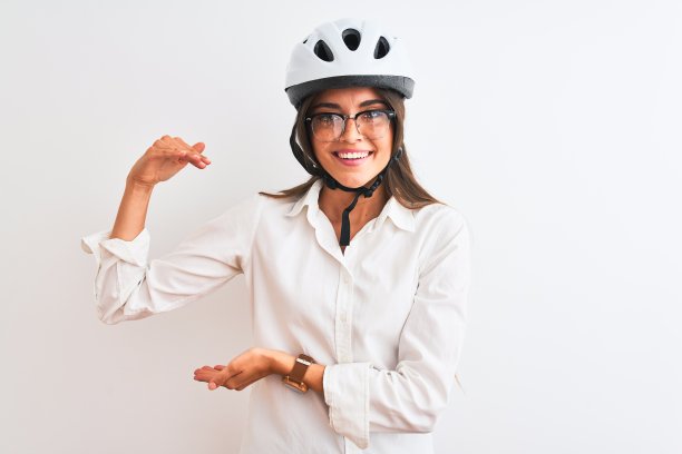 美丽的女商人戴眼镜和自行车头盔在孤立的白色背景手势与手显示大和大尺寸的标志，测量符号。看着镜头微笑。测量的概念。图片下载