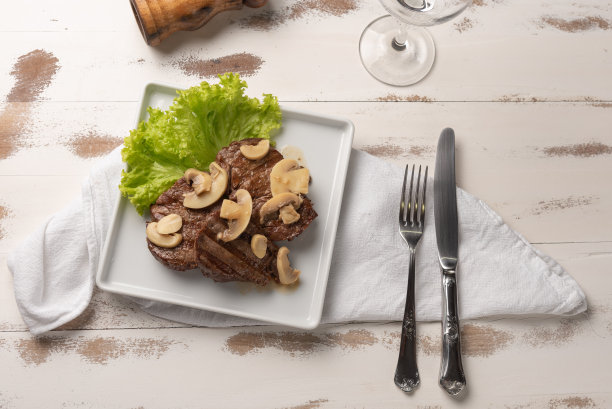 菲力牛排配蘑菇酱，生菜，胡椒粉碎机，木质白色背景，光线柔和图片下载