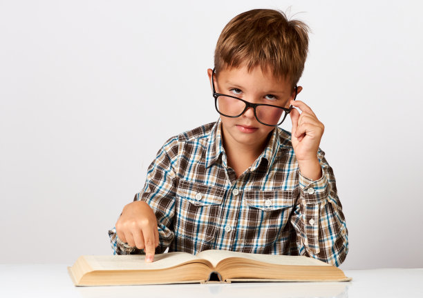 可爱的小男孩拿着书坐在书桌前。七岁的孩子图片下载